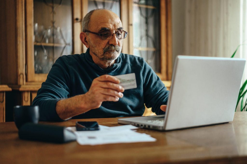 Providence House Senior Living Avoid Senior Scams, Gentleman giving credit card over laptop